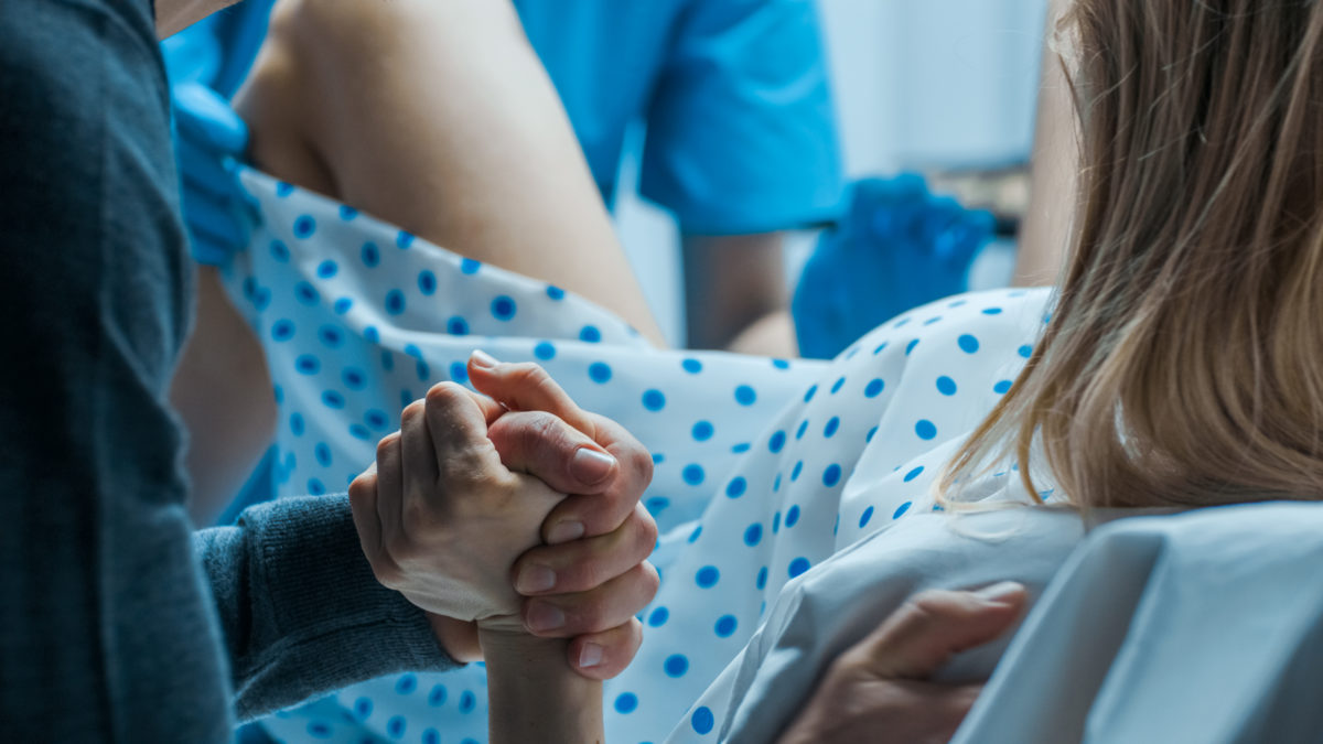woman holding hand of her partner while giving birth in a NY hospital