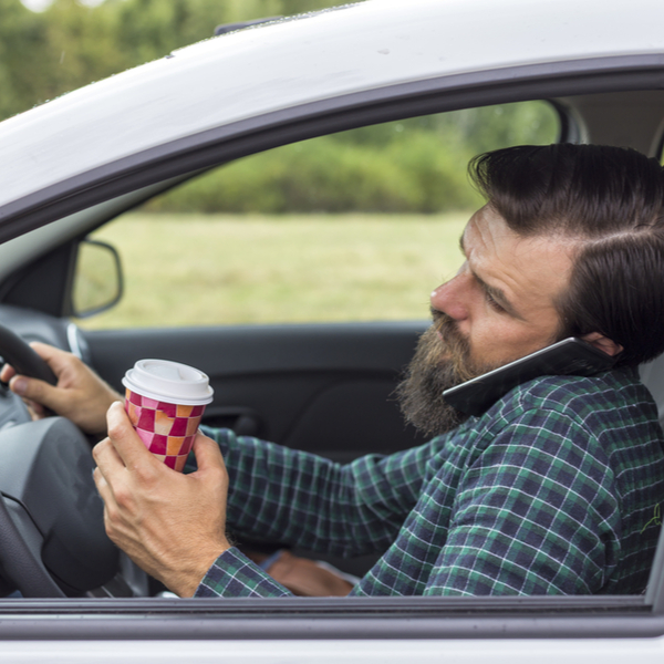 young man drinking and speaking on phone while driving