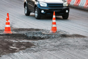 A damaged New York City roadway with orange cones marking a pothole that could cause car accidents.