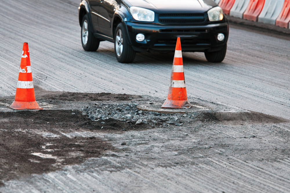 A damaged New York City roadway with orange cones marking a pothole that could cause car accidents.