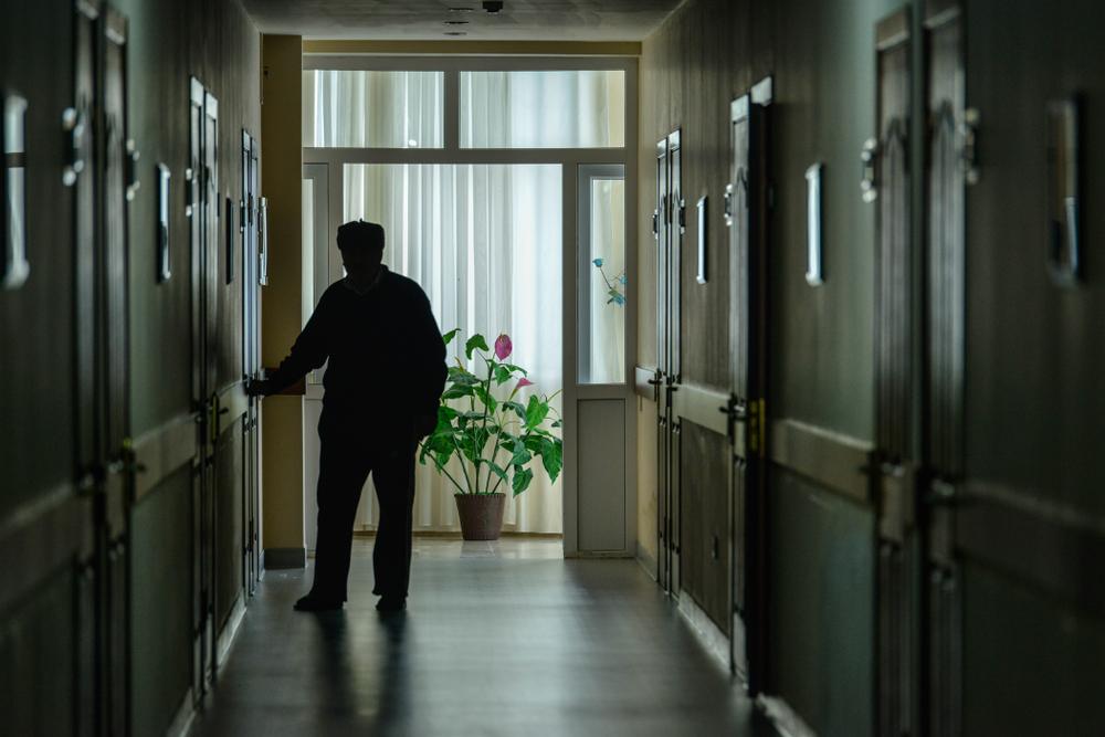 Silhouette of an elderly man standing in a dim nursing home hallway, highlighting unsafe or neglectful conditions in Brooklyn care facilities.