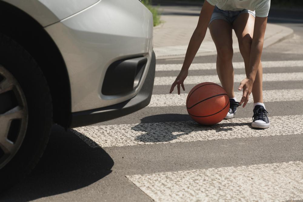 Teenager reaching for a basketball in a Brooklyn crosswalk as a car approaches