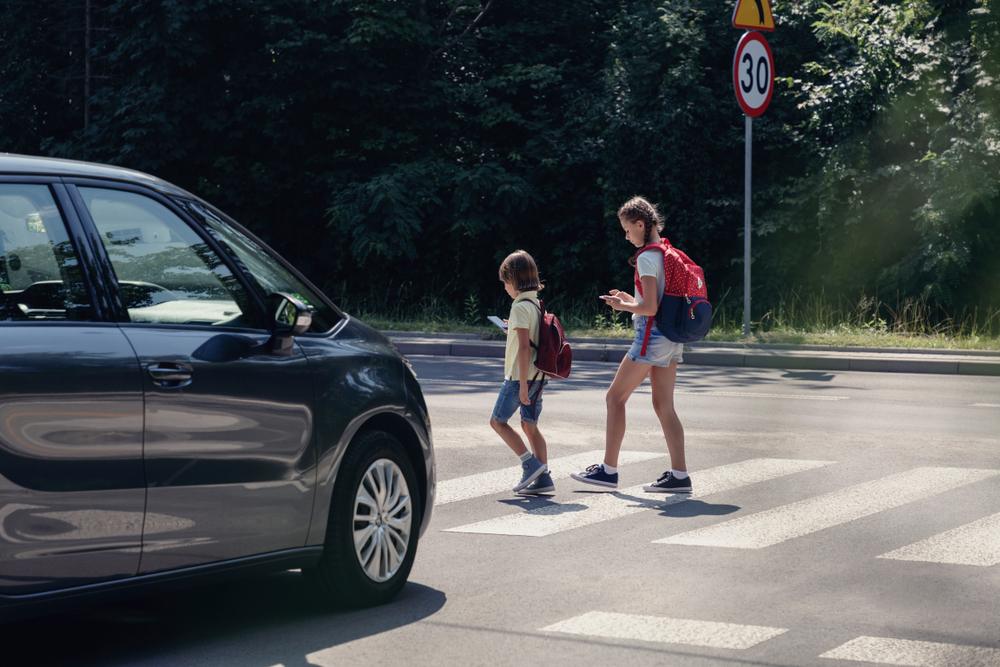 Two children crossing a Brooklyn crosswalk while a vehicle approaches