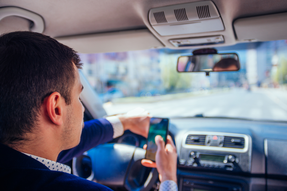 Driver holding a smartphone while driving, showing distracted and unsafe behavior behind the wheel.