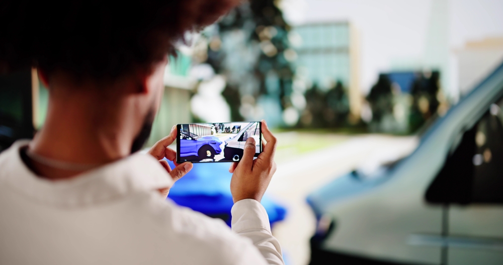 Person taking photos of vehicle damage with a smartphone after a car accident.