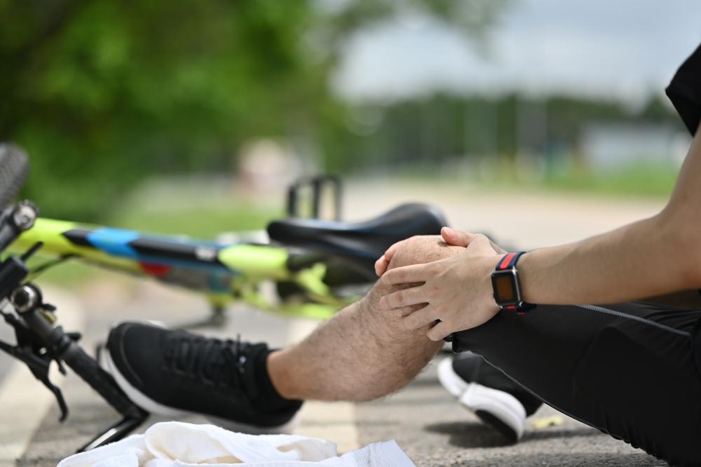 Cyclist sitting on the ground clutching an injured knee after a Brooklyn bike accident.