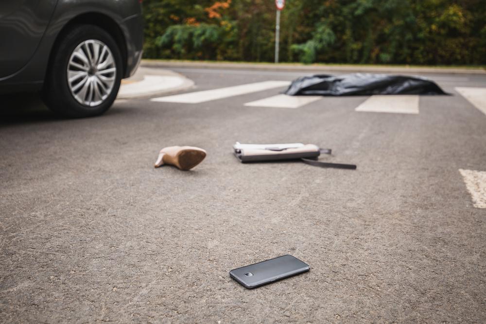 Aftermath of a pedestrian accident in a crosswalk, with personal items scattered on the road