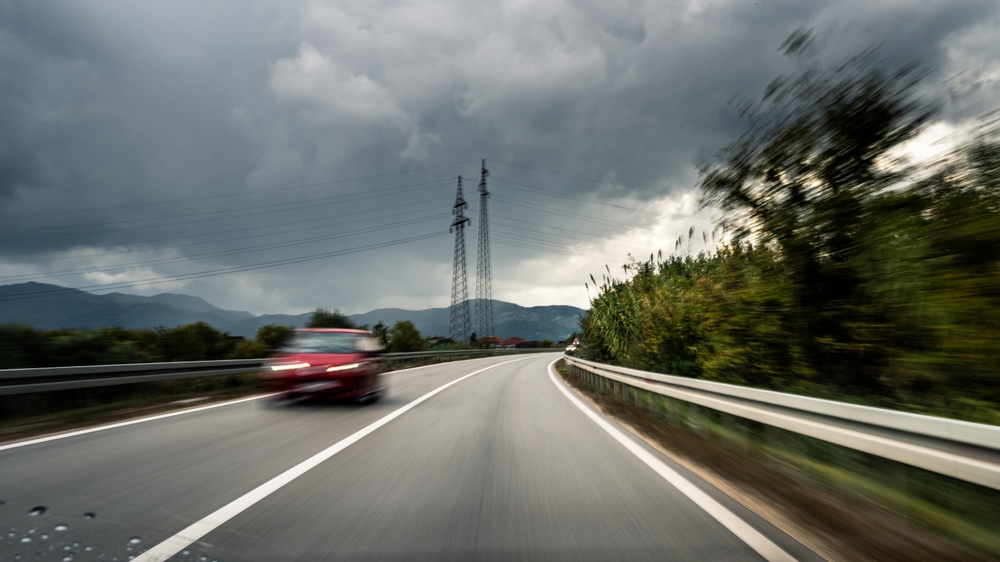 Blurry image of a speeding car on a highway under dark, stormy skies.