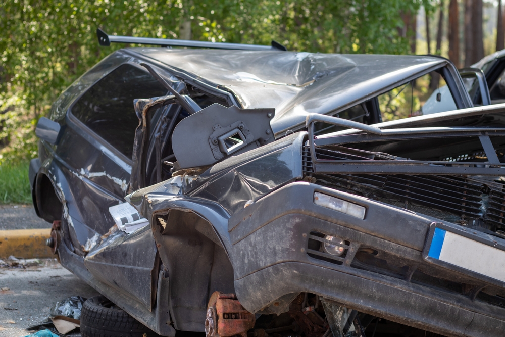 Severely damaged black car after a collision, showing extensive rear and side impact.