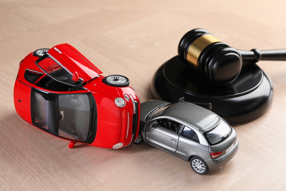 Toy cars in a crash scene beside a judge’s gavel symbolizing legal action after a car accident