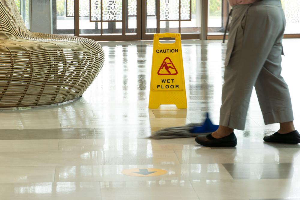Wet floor hazard sign and janitor mopping, showing unsafe conditions that can lead to Brooklyn slip and fall accidents
